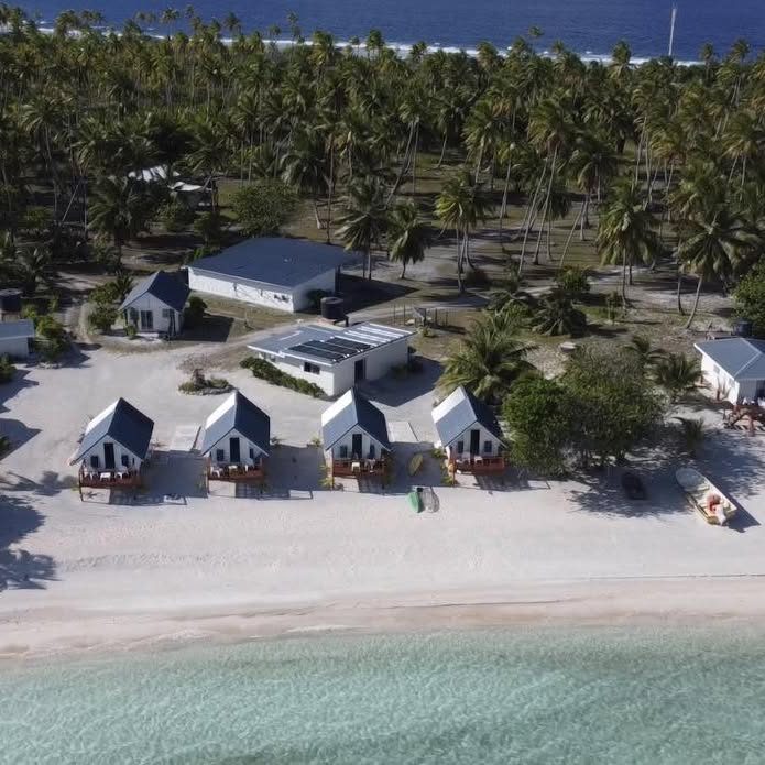 Vue aérienne des bungalows blancs alignés sur le sable, cocoteraie derrière